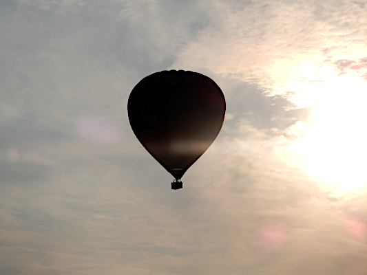 De ballon steekt donker af tegen een helder door de zon verlicht wolkendek.