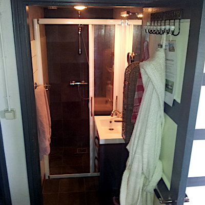 De badkamer met douche, glazen schuifdeur een wastafel met wandmeubel, een spiegel en een badjas.